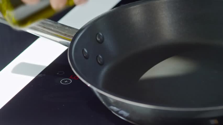 Close-up of a male cook pouring olive oil into a pan on an induction cooker, highlighting cooking, culinary skills, and food preparation.