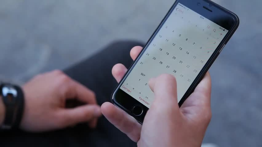 Close-up of male hands scrolling a smartphone screen, navigating a calendar app, illustrating mobile technology, productivity, and daily planning.