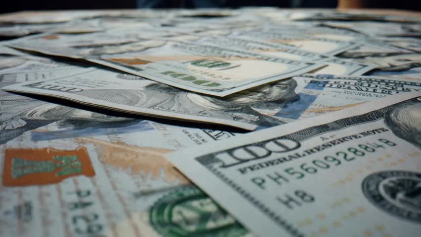Close-up of hundreds of U.S. $100 bills falling on a table, showing cash, American currency, Benjamin Franklin portrait, and money heap.