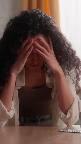 Tired suffering Hispanic Caucasian woman at home kitchen drink pill glass water headache symptom medicine health problem female girl drinking drug indoor ill sick head ache pain painkiller migraine