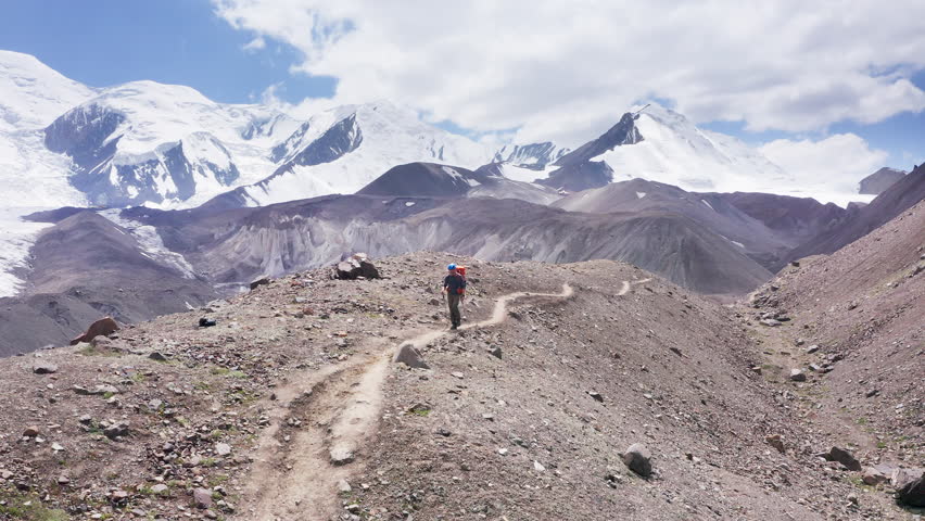 Lonely Climber in mountaineering Gear, backpack and trekking poles during Lenin peak descending with mountain peaks in background. Extreme active people, high-altitude mountaineering 4`k concept