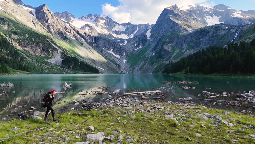 a girl with a backpack is walking along the shore of a mountain lake