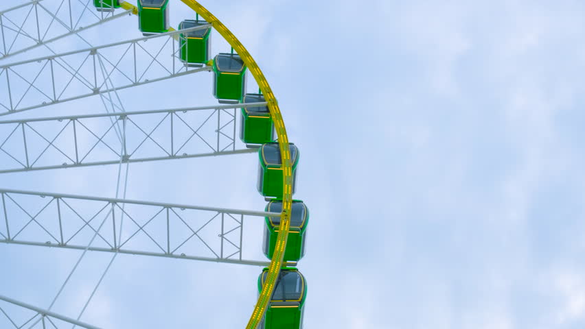 Ferris wheel in amusement park with colorful lights. Part of turning ferris in theme park with unrecognizable people. Below angle medium shot on mid day real time shot with copy space area.