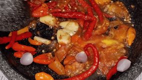 A hand grinds fresh ingredients—red chilies, shallots, garlic, shrimp paste, salt, and tomato—meticulously in a stone mortar (cobek). - Powered by Shutterstock - Get 15% off with code: PIKWIZARD15