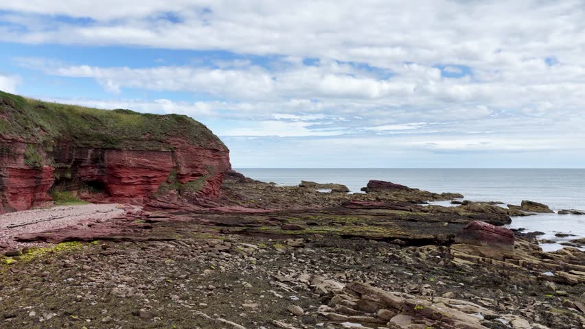 Camera slowly pans revealing red sandstone cliffs, layered rocks, and North Sea under soft daylight