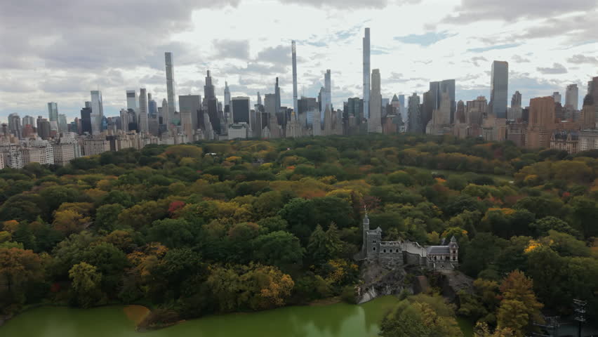 Cinematic Aerial scene of Manhattan Central Park in New York City, New York showing green canopy, winding paths and surrounding midtown skyline under clear daylight from a high perspective.