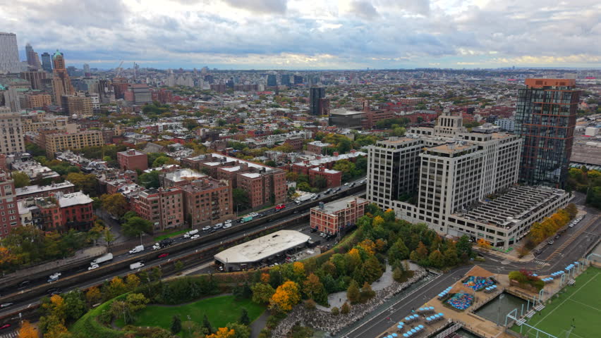 High aerial view of New York City, Brooklyn, New York showing residential buildings, tree lined streets and a soft cloudy skyline stretching far across the urban landscape.