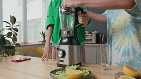 Two gen Z Caucasian teenagers standing at kitchen counter, turning on blender to make fruit smoothie - Powered by Shutterstock - Get 15% off with code: PIKWIZARD15