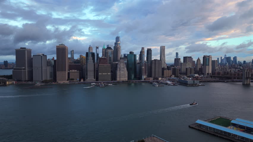 Aerial drone shot of New York City, New York showing tall downtown buildings, open riverfront areas and textured cloudy light creating a wide panoramic city atmosphere.