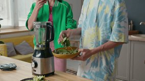 Caucasian teen girl holding smartphone recording video of her teen boyfriend adding spinach into blender while cooking smoothie - Powered by Shutterstock - Get 15% off with code: PIKWIZARD15