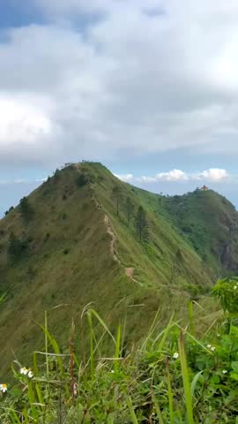 Stunning panoramic view of steep, grassy green hills with a clear trekking path under a cloudy blue sky