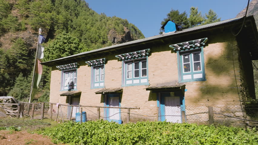 Drone rising over a teahouse, revealing a river town between mountains of Nepal