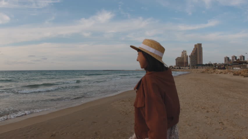 A happy woman runs to the sea along a sandy beach and looks at the camera. The girl is in a romantic mood. A girl on the beach.