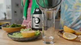 Close-up of unrecognizable boy pouring fresh homemade smoothie from blender container into glass on kitchen counter, girl standing in background - Powered by Shutterstock - Get 15% off with code: PIKWIZARD15