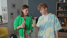 Medium portrait of Caucasian teenagers clinking glasses with homemade smoothie, drinking it and smiling at camera while standing in kitchen - Powered by Shutterstock - Get 15% off with code: PIKWIZARD15