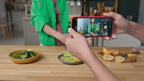 Teen boy holding smartphone in hands, recording video of girl influencer making smoothie via blender in kitchen - Powered by Shutterstock - Get 15% off with code: PIKWIZARD15