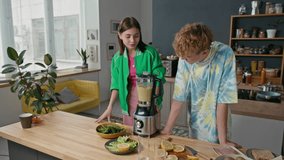 Modern teen siblings wearing stylish casual clothes standing at kitchen counter, preparing fruit smoothie via blender - Powered by Shutterstock - Get 15% off with code: PIKWIZARD15