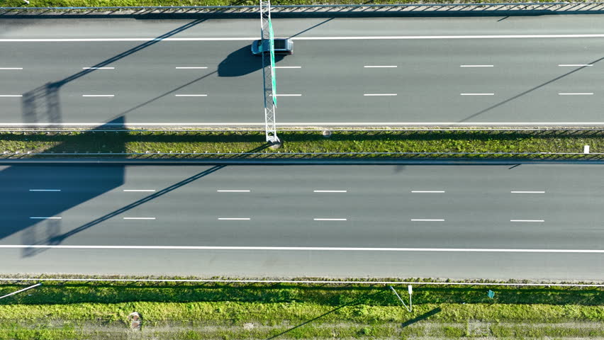 Top-down drone view of vehicles traveling on a highway with structural shadows cast across the lanes.