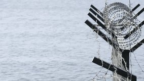 Razor and barbed wire atop a coastal security fence against a gray sea, symbolizing border control, restricted zones, maritime protection, confinement and divided territory - Powered by Shutterstock - Get 15% off with code: PIKWIZARD15