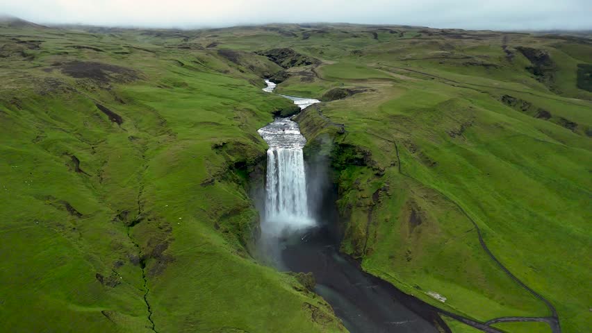 Experience the awe-inspiring beauty of Skogafoss Waterfall, a stunning natural wonder in Iceland. Water flows powerfully over cliffs, surrounded by vibrant greenery, showcasing natures magnificence.