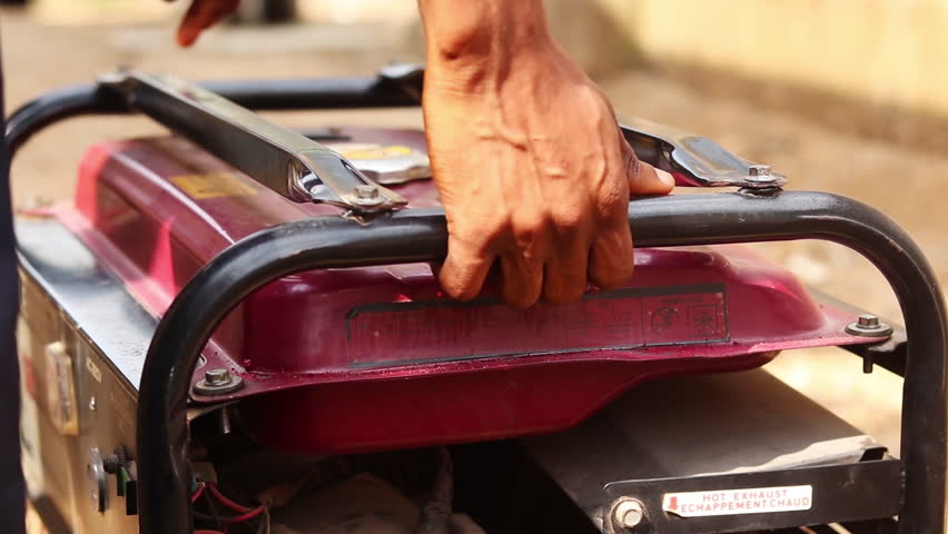 Man picking up a handheld power generator and walking away. Footage of a man lifting and carrying a gasoline general on a sunny day.