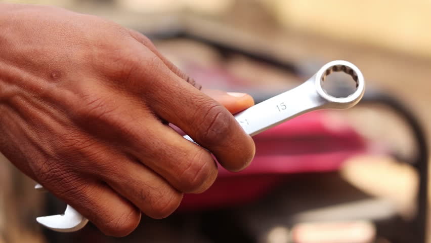 Close up of a man showing a ring socket wrench while standing in front of a gasoline fuel generator