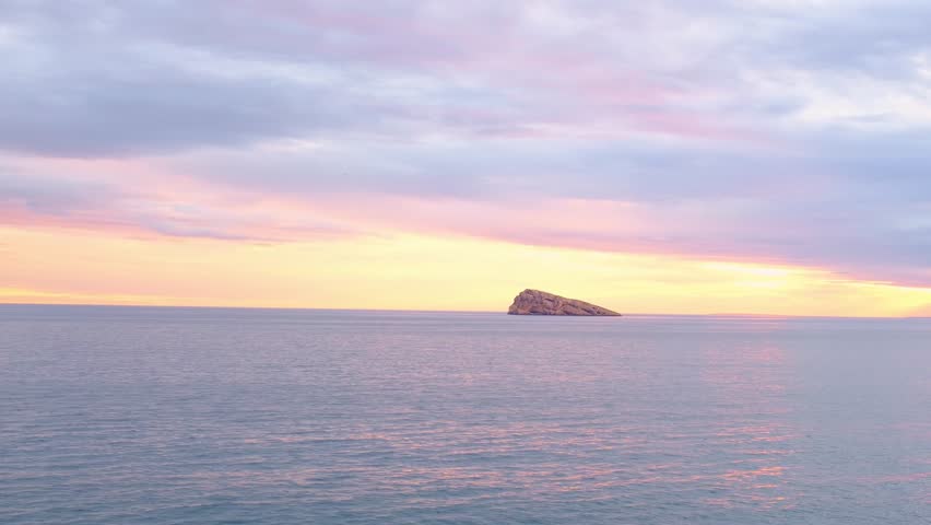 Sunset view over Cala Tio Ximo and Benidorm island. Tranquil winter sea, soft sunset glow, peaceful view of small island near Benidorm. Quiet natural beauty, no people, only sea and sky.