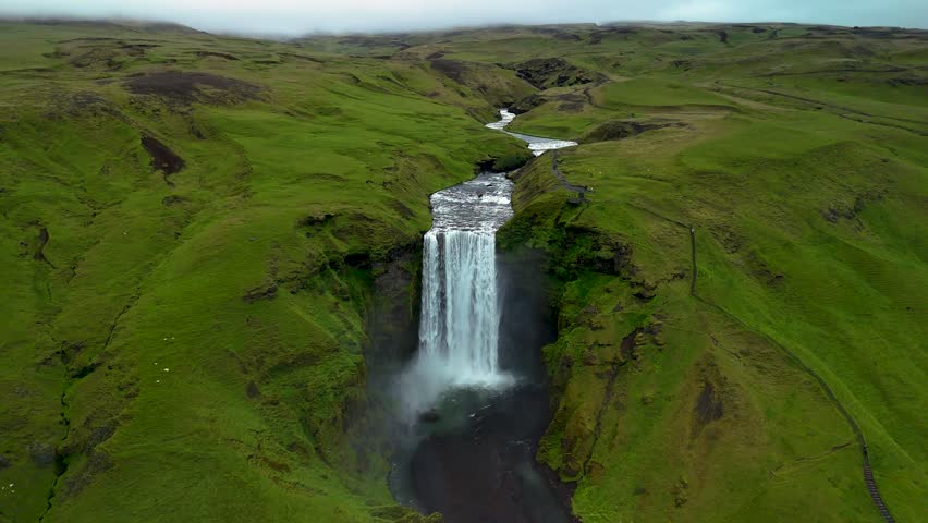 Experience the breathtaking beauty of Skogafoss Waterfall in Iceland. Water plunges powerfully over cliffs, surrounded by vibrant green hills and a serene atmosphere. A true natural wonder awaits.