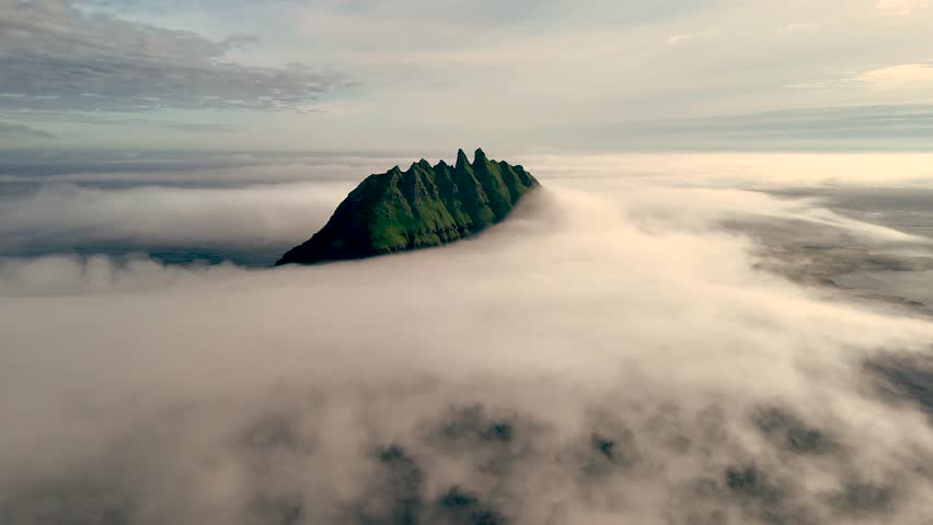 Witness the stunning Drangarnir islets emerging dramatically from a sea of clouds during sunrise in the Faroe Islands, showcasing natures beauty and tranquility.