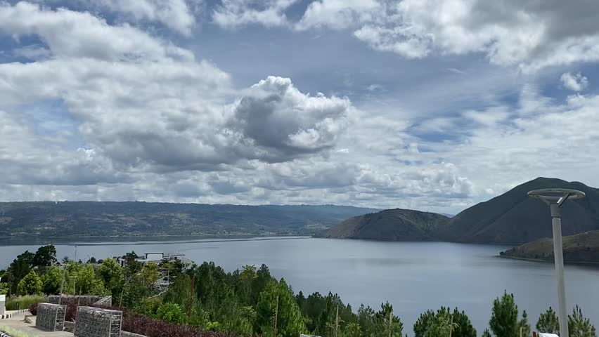 High-angle view of lake and mountains with dramatic cloud movement under bright daylight.