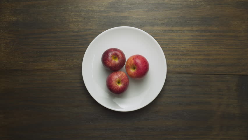 Woman hands are wrapping fresh ripe apples in cling film. Red fruits on white plate wrapped in plastic wrap. Food freshness concept. Protection for food.