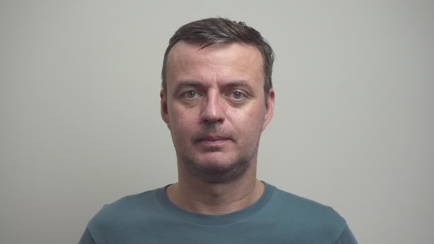 Middle-aged man is putting on sunglasses. Portrait of satisfied person in sunglasses on white wall background.