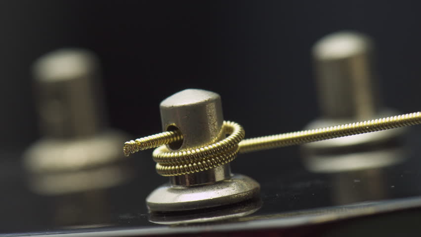Closeup view of winding a new string onto a guitar tuning peg. Part of musical string instrument. Detail of acoustic guitar.