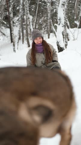 A young woman relaxes during a walk in a winter forest with her dog.