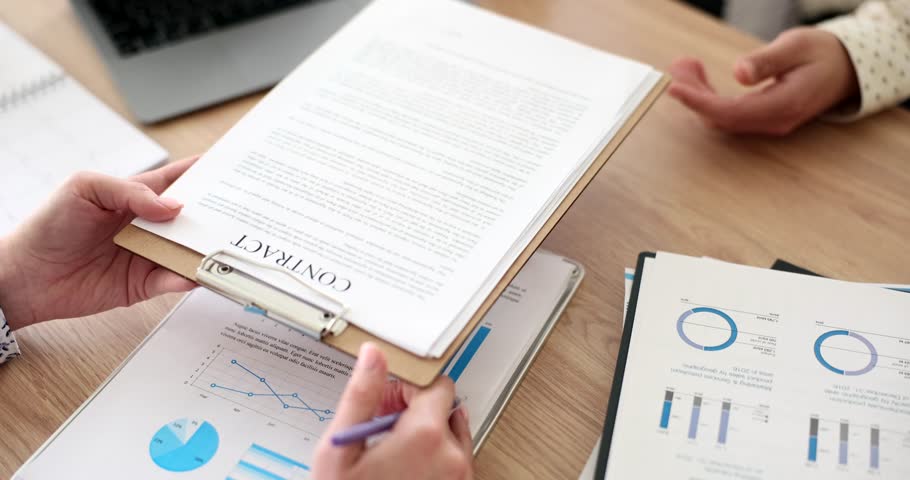 Experienced businesswoman presents contract to partner for review. Businessman sits at desk and studies obligations and terms with attention to detail