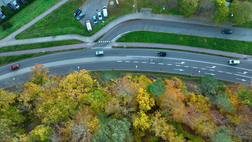 Overhead aerial drone shot of a curved road with traffic and pedestrian crossing next to autumn trees in Gdansk Oliwa.