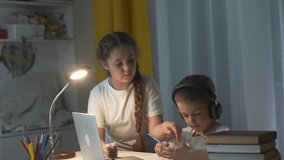 Woman and child sitting at desk with laptop. Schoolchildren are learning how to use laptop in distance. Children studying on table in the evening. A girl and a lifestyle woman are seated at a desk. - Powered by Shutterstock - Get 15% off with code: PIKWIZARD15