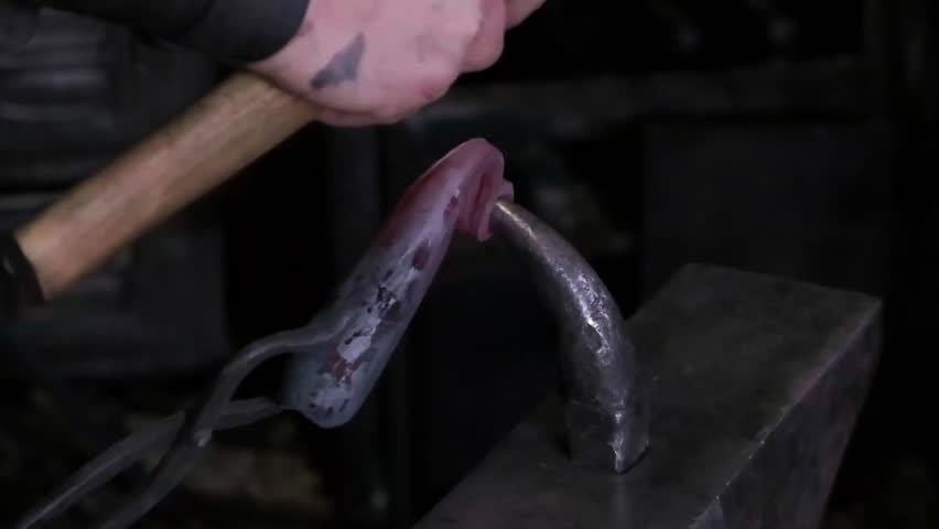 Blacksmith hands hammering hot glowing steel on anvil closeup traditional metal forging workshop