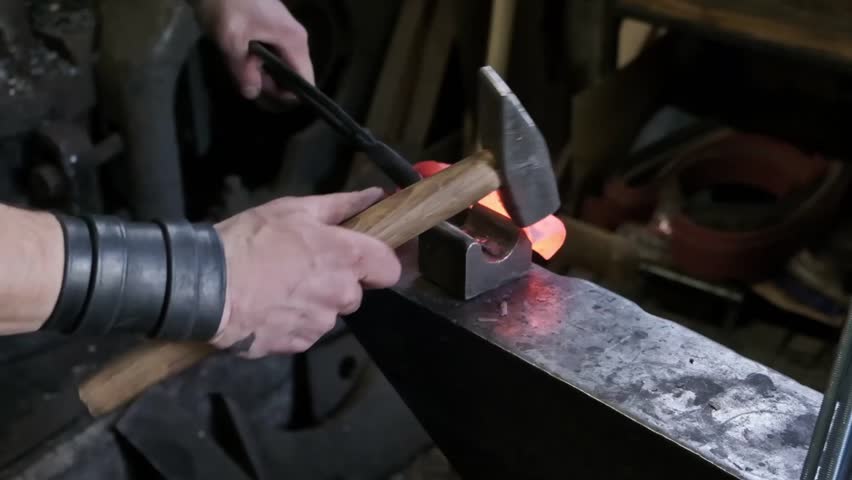 Blacksmith hands hammering hot glowing steel on anvil closeup traditional metal forging workshop