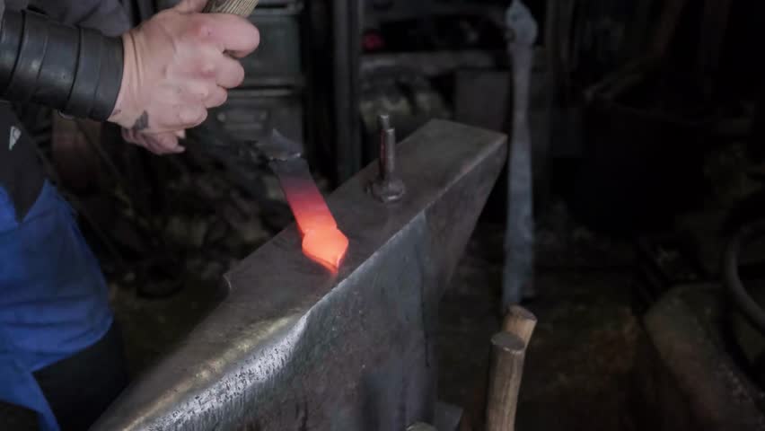 Blacksmith hands hammering hot glowing steel on anvil closeup traditional metal forging workshop