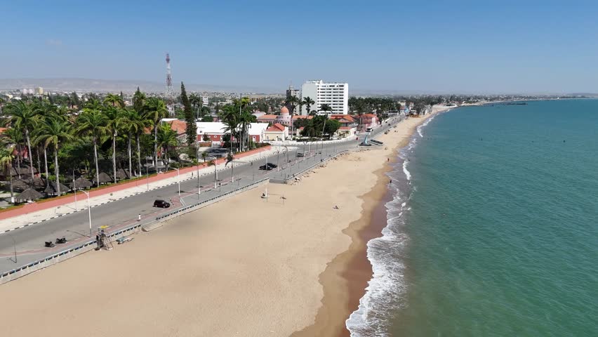 Aerial panorama of Benguela city, Angola, showing long sandy coastline, waterfront avenue, and palm trees separating town life from the beach below