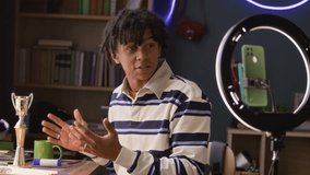 Medium shot of gen Z athletic boy talking about medals and trophies on camera of smartphone in ring light holder while streaming at home - Powered by Shutterstock - Get 15% off with code: PIKWIZARD15