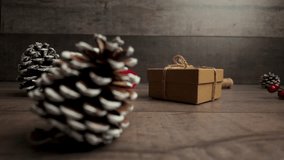 Slow motion holiday scene showing a kraft paper gift and pine cone on a wooden surface as the camera smoothly moves to the right - Powered by Shutterstock - Get 15% off with code: PIKWIZARD15