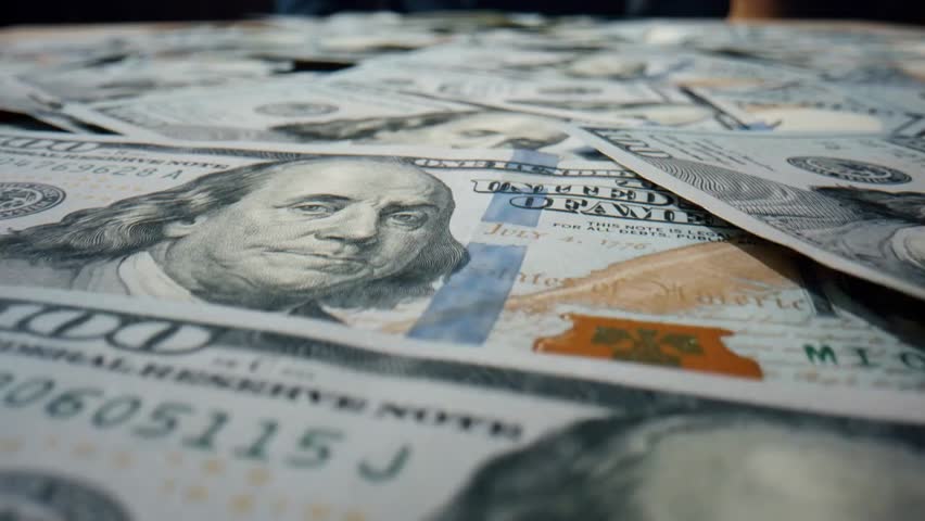 Close-up macro view of scattered hundred-dollar banknotes lying on a table, showing detailed textures, Benjamin Franklin portrait, and concepts of money and finance.