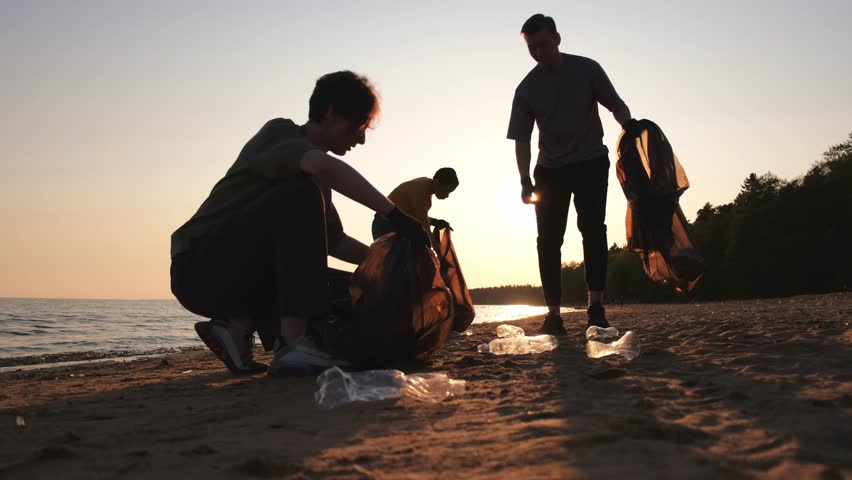 Earth day. Volunteers activists collects garbage cleaning of beach coastal zone. Woman and mans puts plastic trash in garbage bag on ocean shore. Environmental conservation coastal zone cleaning