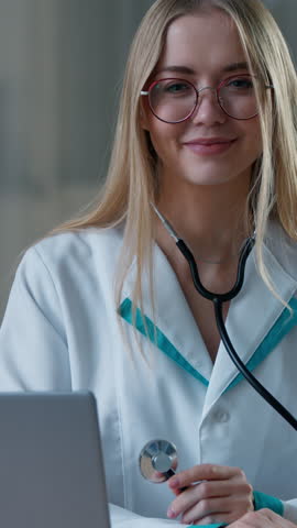 Caucasian woman female doctor posing in clinic showing stethoscope medical equipment in hospital at table with laptop computer girl nurse working looking at camera smiling pediatrician cardiologist