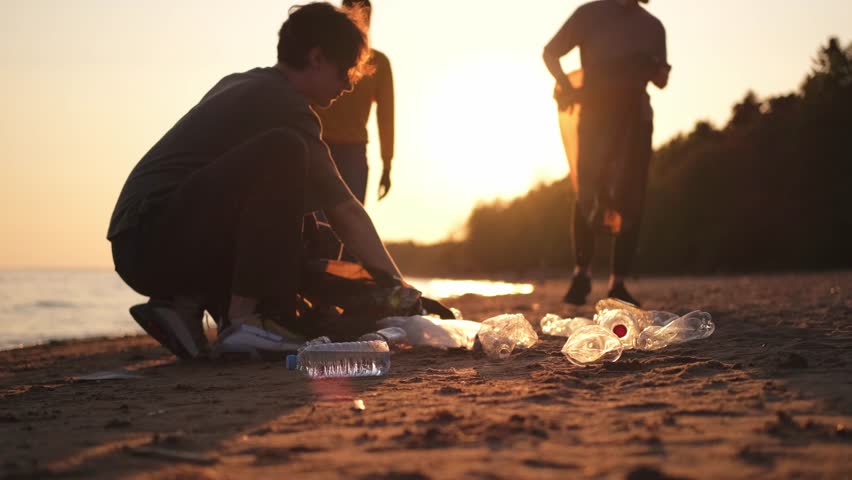 Earth day. Volunteers activists collects garbage cleaning of beach coastal zone. Woman and mans puts plastic trash in garbage bag on ocean shore. Environmental conservation coastal zone cleaning
