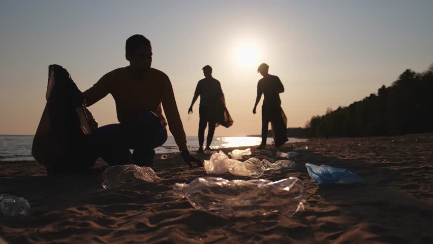 Earth day. Volunteers activists collects garbage cleaning of beach coastal zone. Woman and mans puts plastic trash in garbage bag on ocean shore. Environmental conservation coastal zone cleaning