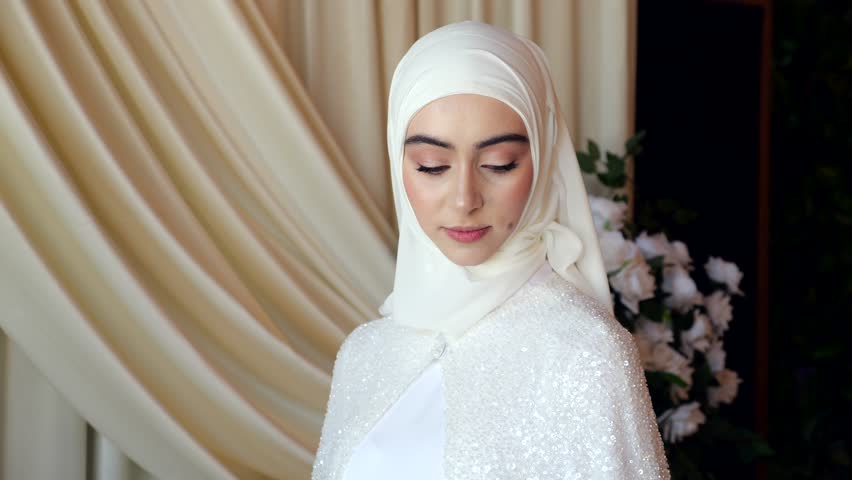 Chechen bride in hijab looks to the side standing by elegant wedding drapery