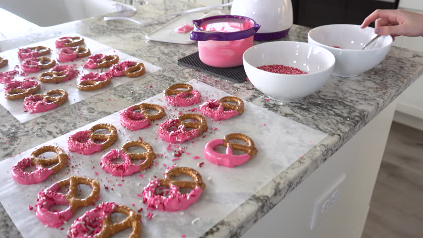 With focused attention, this budding culinary artist dips pretzels into a pot of melted chocolate, creating sweet delights in the warmth of a well-lit home kitchen.